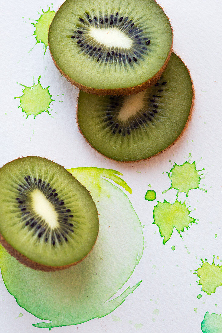 Kiwi slices on a paper background with green splashes of colour