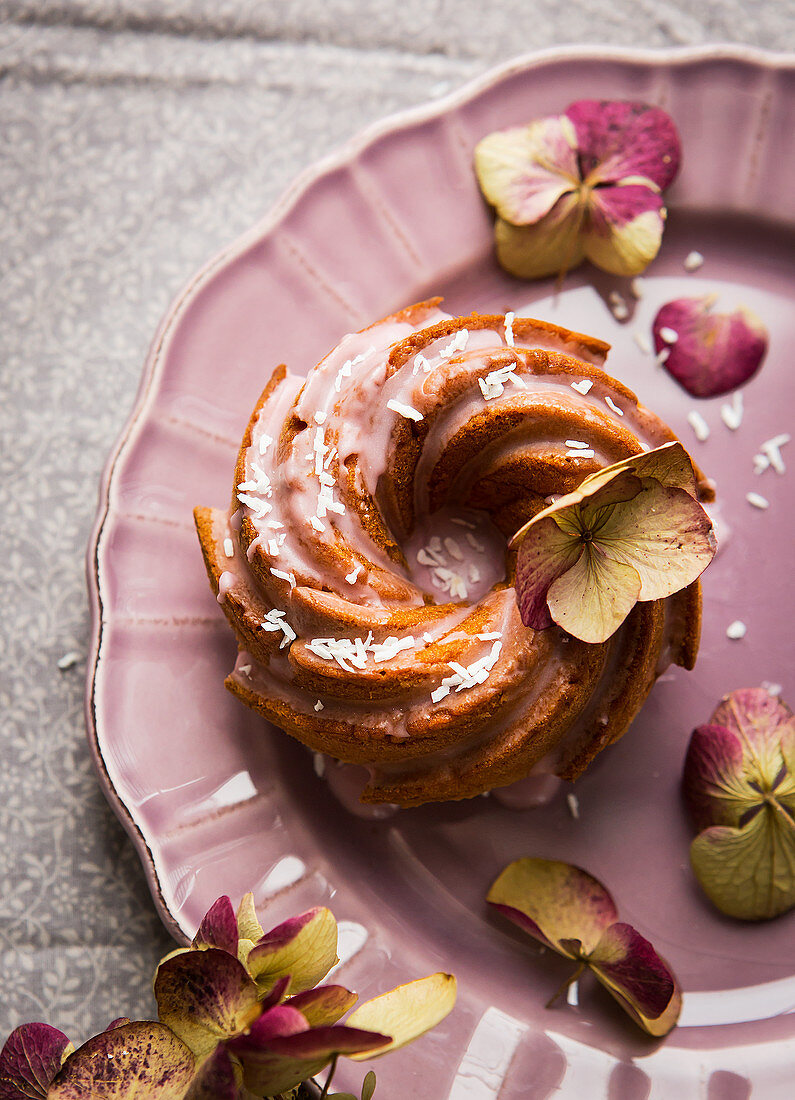 Mini wreath cake with icing and dried flowers on a pink plate