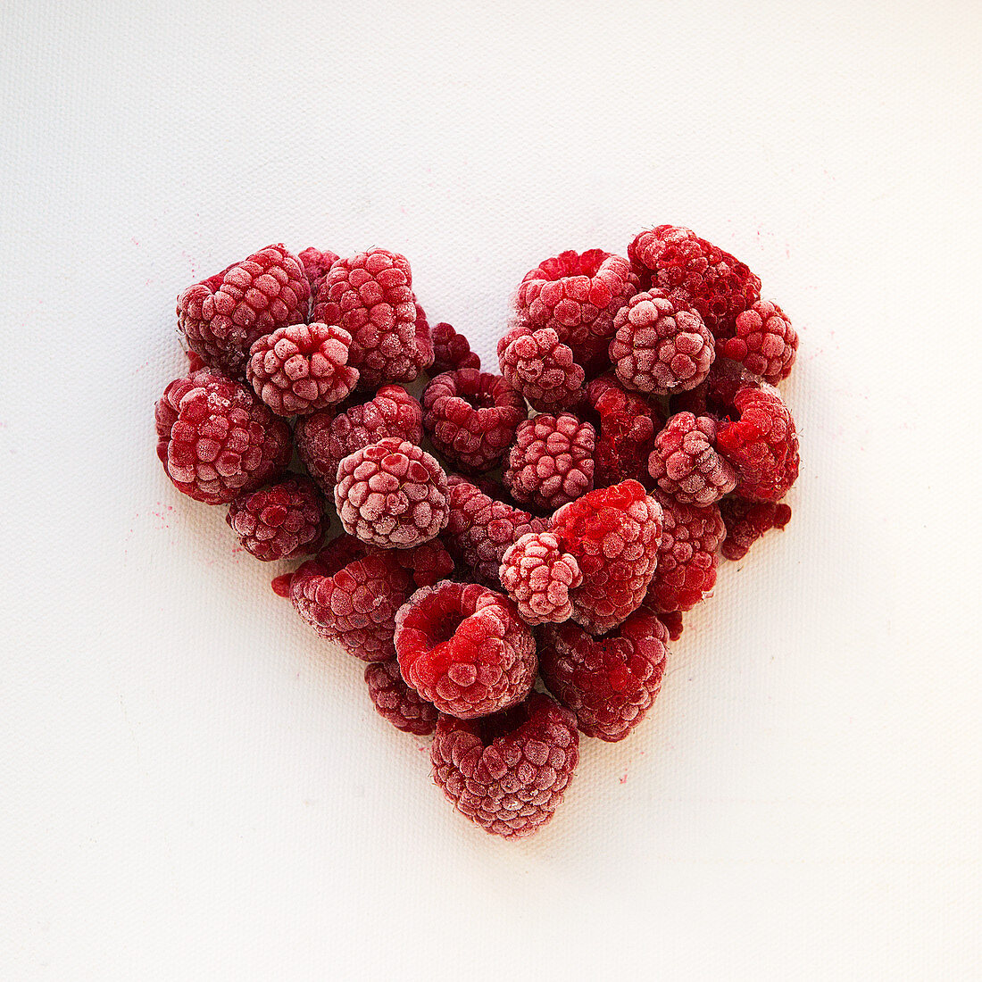 A heart of frozen raspberries on a white background