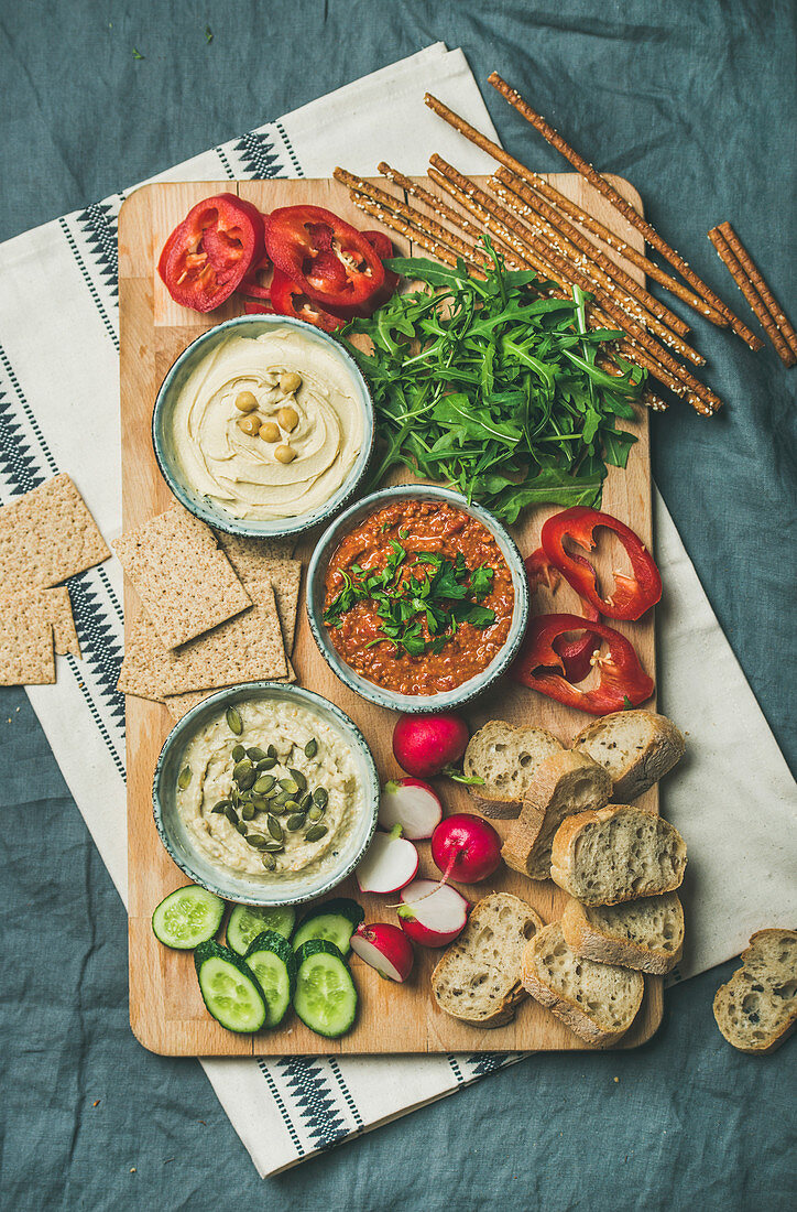 Various Vegetarian dips: Hummus, babaganush and muhammara with crackers, bread and fresh vegetables on wooden board