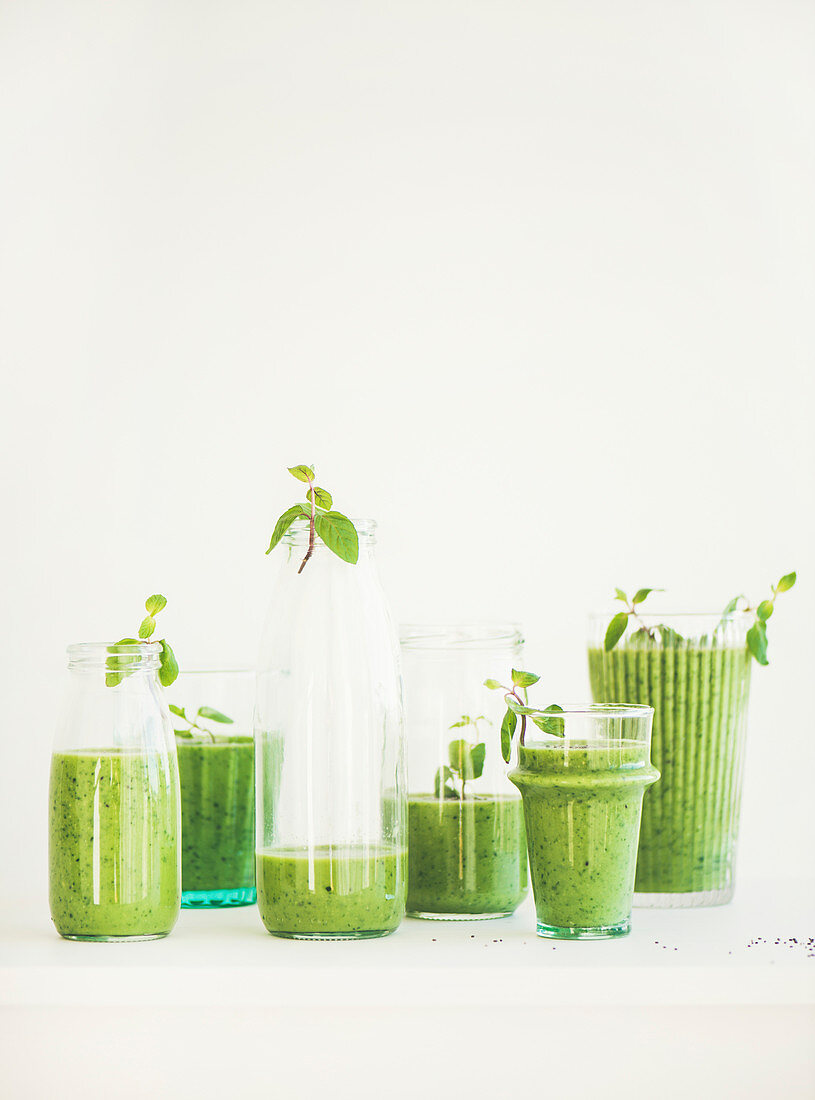 Matcha green vegan smoothie with chia seeds and mint in glasses and bottles over white background