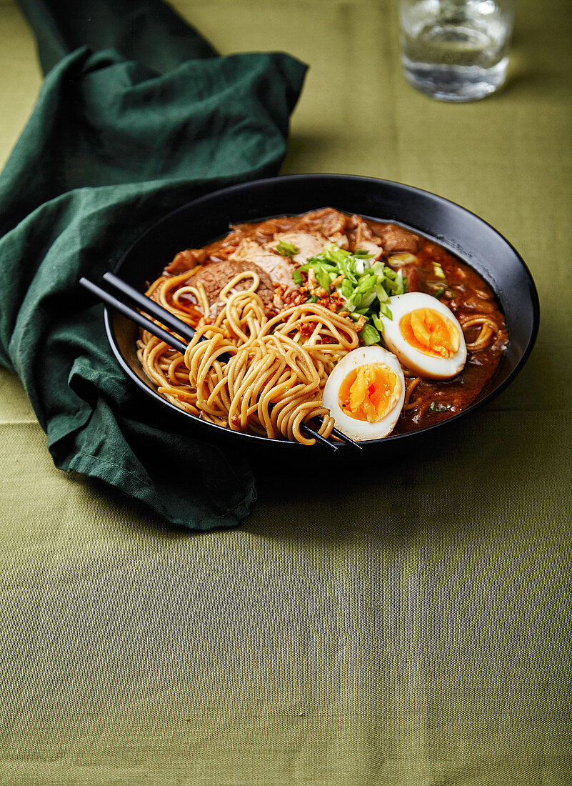 Japanese ramen with pork belly, mushrooms and marinated eggs on green linen tablecloth