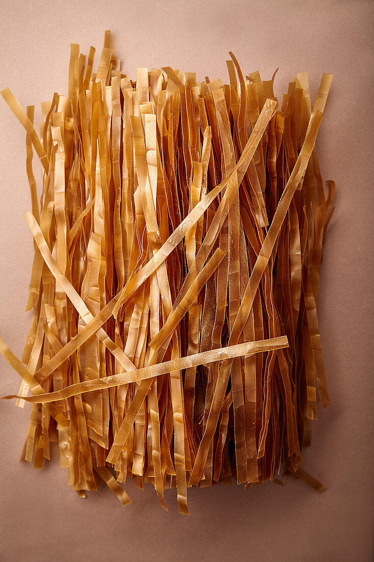 Heap of red rice noodles made with coconut milk on brown background