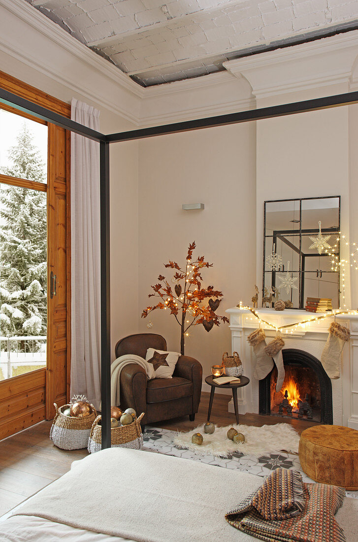 Cosy armchair and open fireplace with four-poster bed in foreground