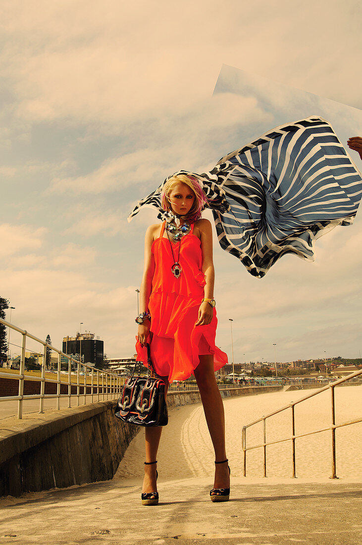 A blonde woman wearing an orange summer dress and a black-and-white sarong