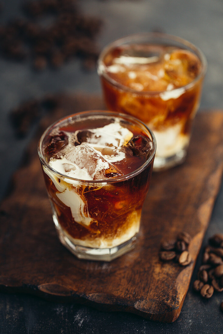 Two glasses of iced coffee with milk on a wooden board
