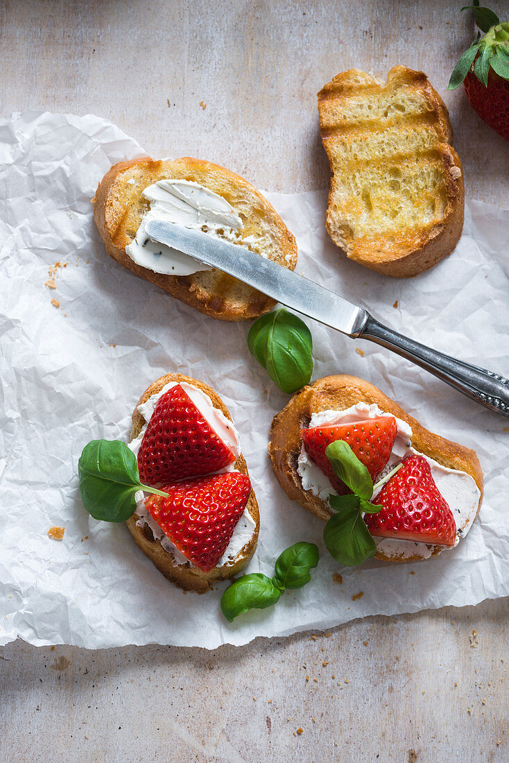 Toasted baguette slices with almond cream cheese, strawberries and basil (vegan)