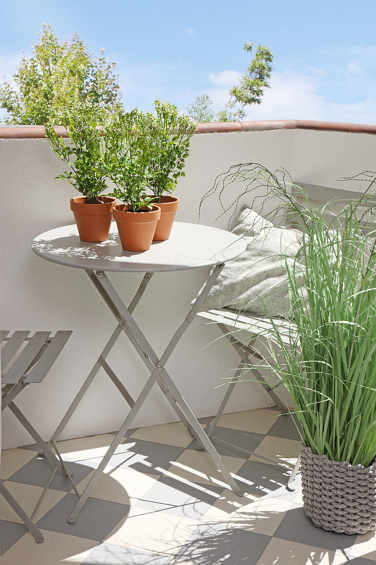 Grey folding table and chairs on balcony with patterned floor tiles and plants