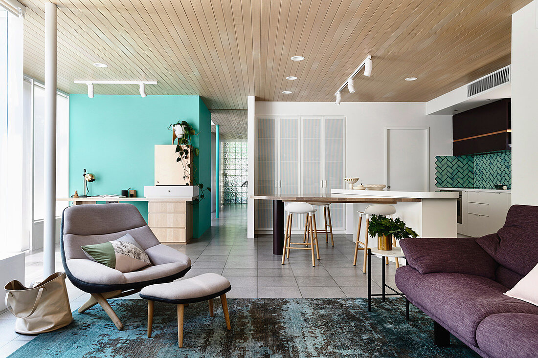 Purple sofa and designer armchair with ottoman in open living room