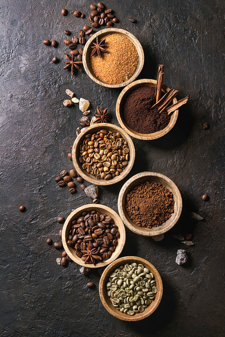 Variety of grounded, instant coffee, different coffee beans, brown sugar, spices in wooden bowls over dark texture background