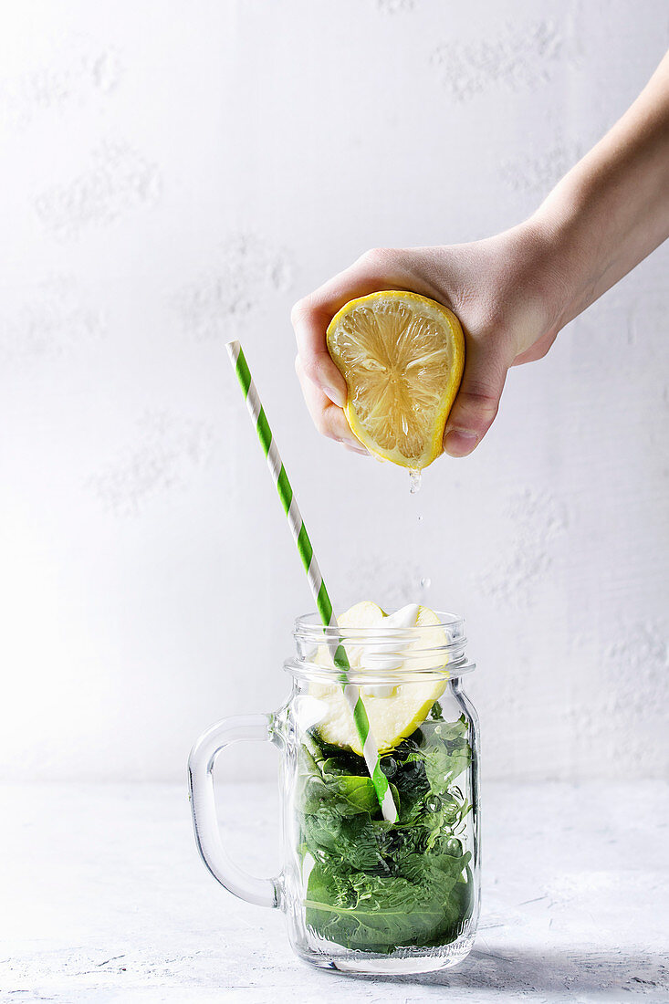 Gepresster Zitronensaft tropft in Glas mit Zutaten für Apfel-Spinat-Smoothie