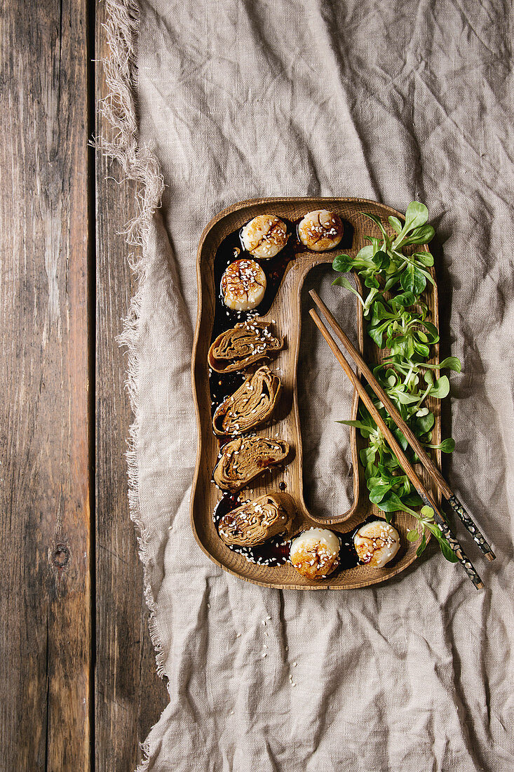 Asian style fried scallops with Japanese Rolled Omelette Tamagoyaki and soy sesame sauce in wooden plate with green salad, chopsticks