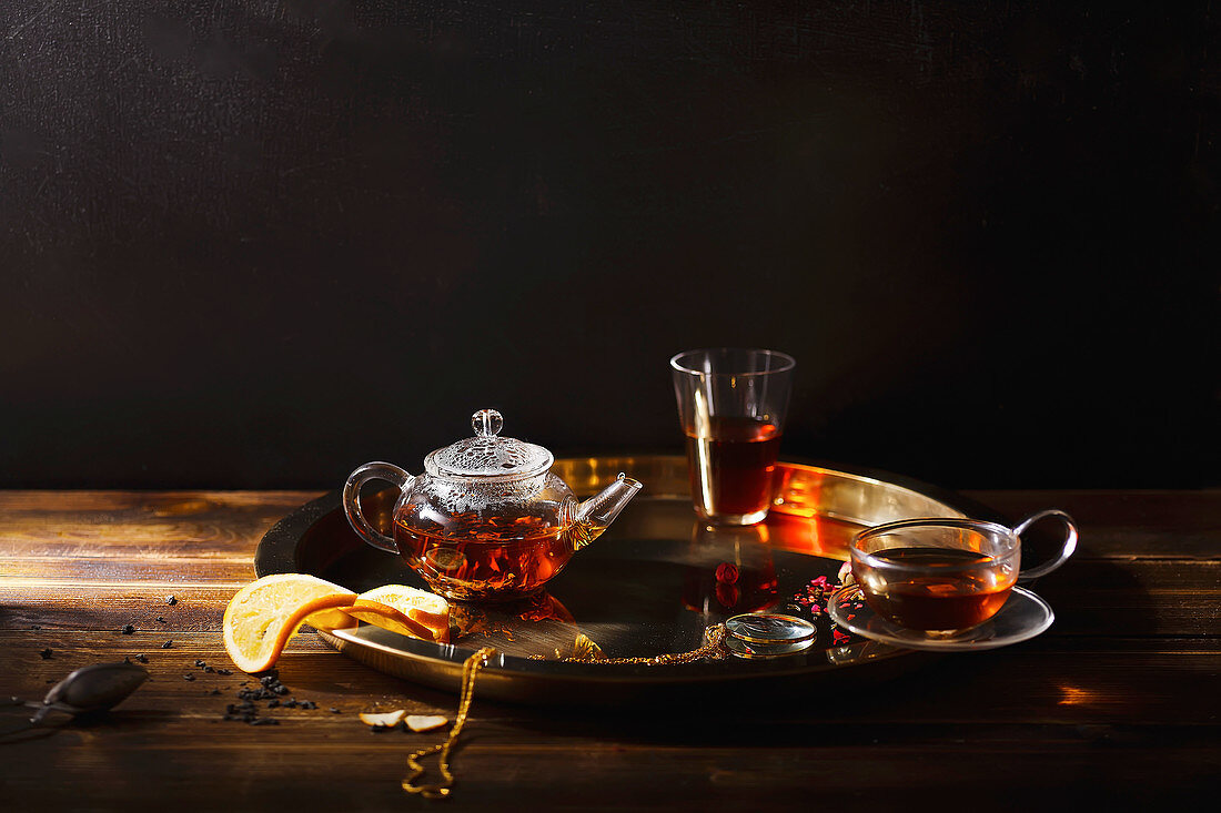 Teatime: Glasteekanne, Teeglas und Teetasse auf goldenem Tablett