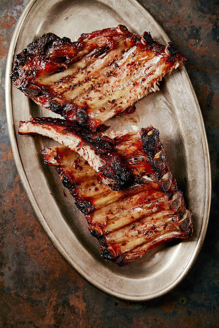 Flavorful grilled pork ribs in thick barbeque sauce cut in messy way served in vintage metal tray