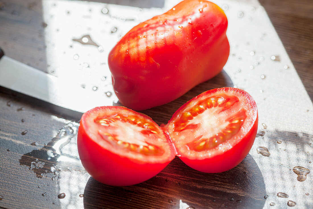 Eine ganze und eine halbierte Tomate auf sonnigem Tisch im Freien