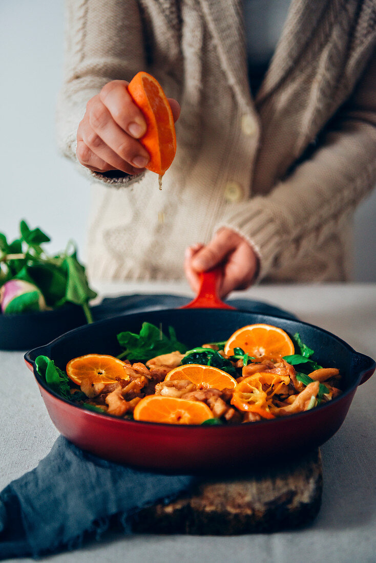 A woman squeezing orange over a chicken meal cooked with orange and spinach