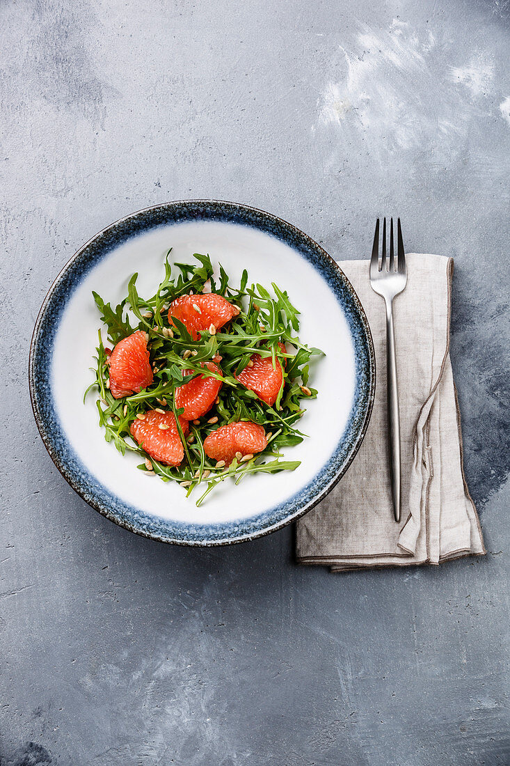 Arugula salad with Grapefruit and sunflower seeds on gray concrete background