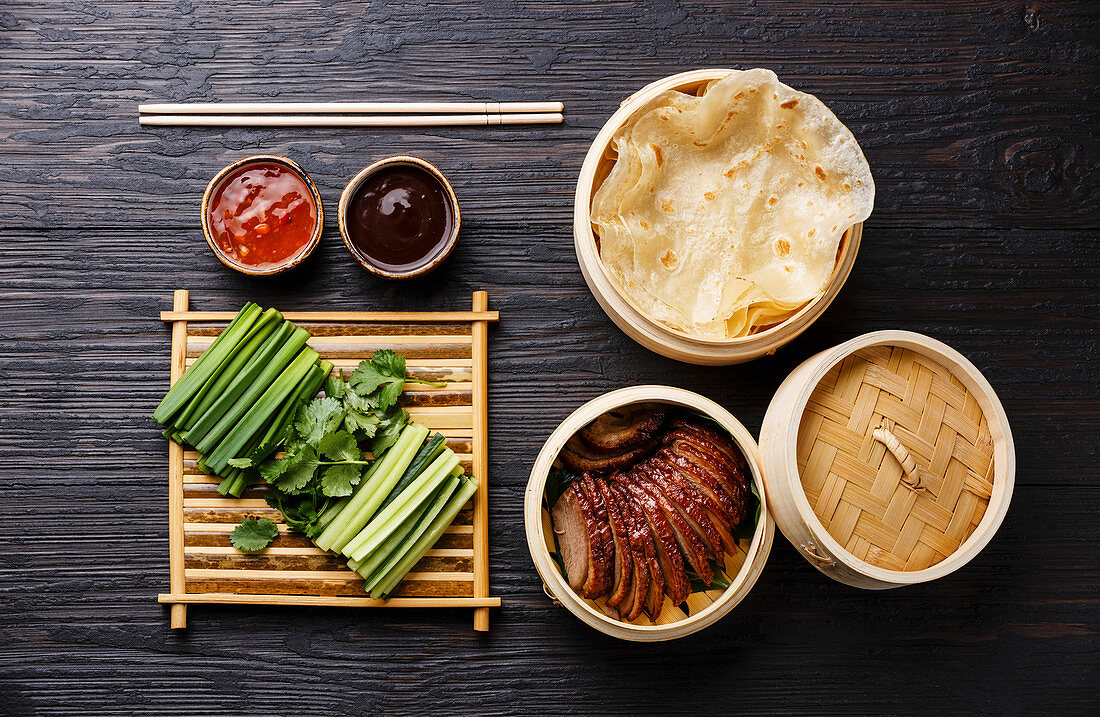 Sliced Peking Duck in bamboo steamer served with fresh cucumber, green onions, cilantro and roasted wheaten chinese pancakes with sauce Hoysin