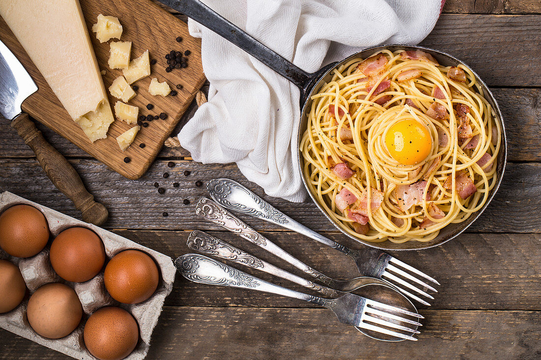 Spaghetti Carbonara mit Zutaten auf rustikalem Holzuntergrund (Aufsicht)