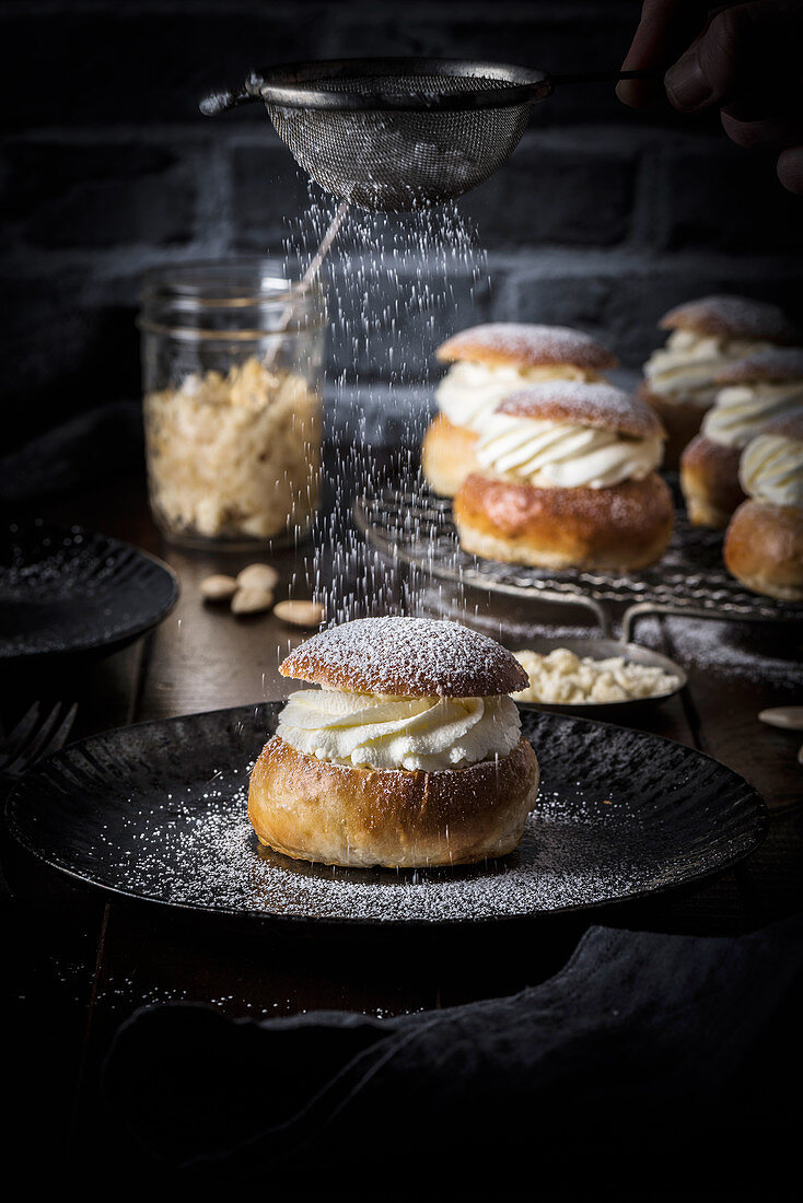 Cream buns on a plate being dusted with icing sugar