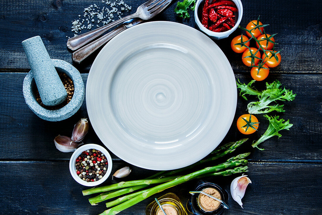 Various colorful spices and vegetables around empty plate on rustic wooden background