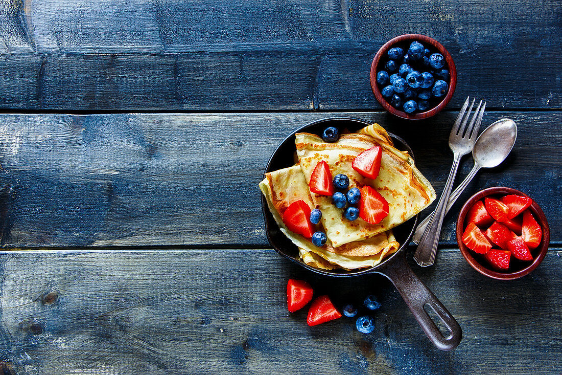 Crepes with fresh berries on rustic wooden background