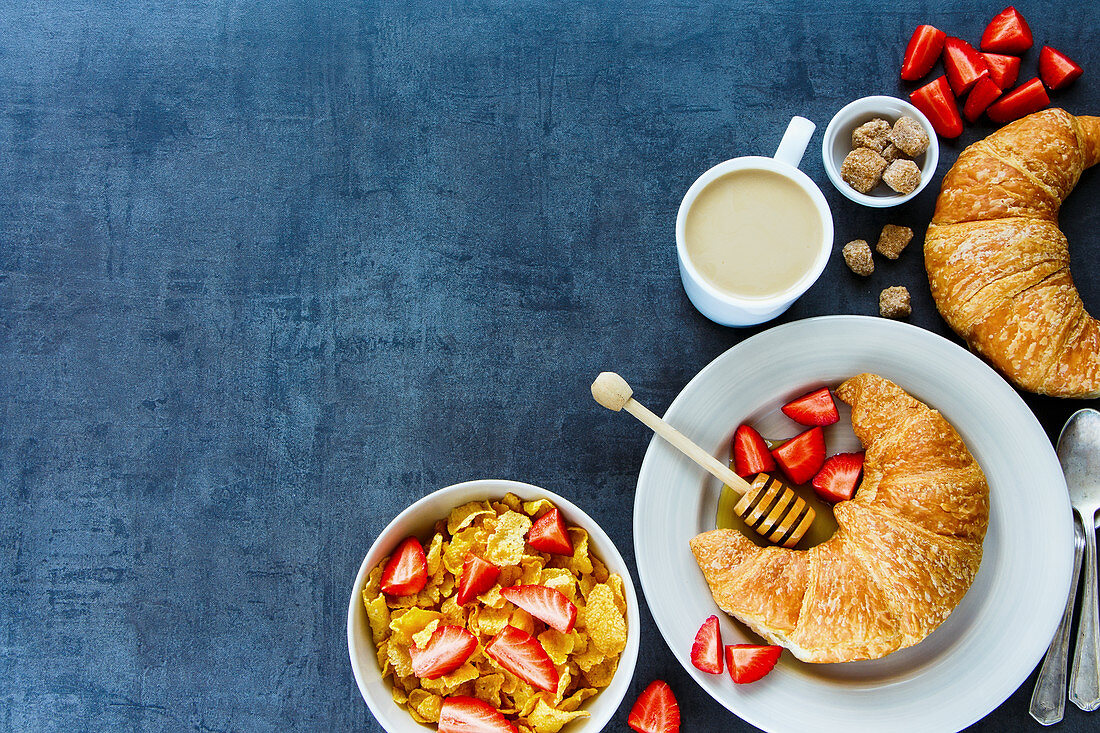 Frühstückstisch mit Cornflakes, Croissants, Honig, Erdbeeren und Kaffee