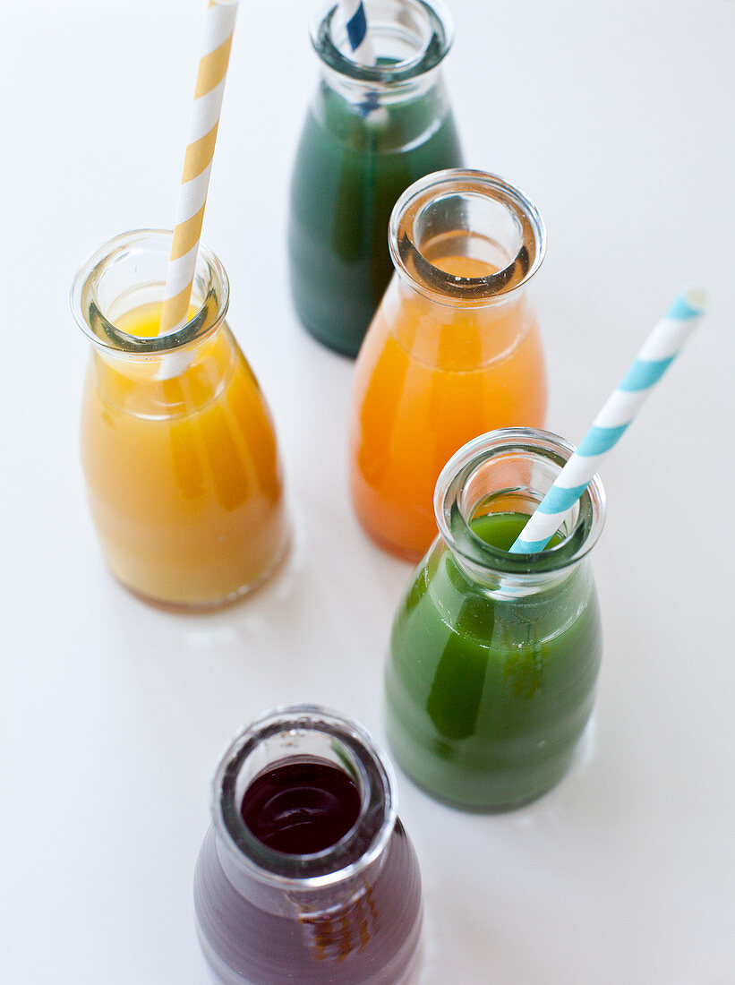 Verschiedene frisch gepresste Säfte in Flaschen mit Strohhalm (Spinatsaft, Zitronen-Ingwer, Spirulina, Orangen-Möhren-Saft mit Kurkuma und Rote-Bete-Saft)