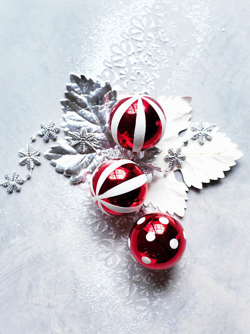 Rot-weiße Christbaumkugeln auf silbernen Blättern