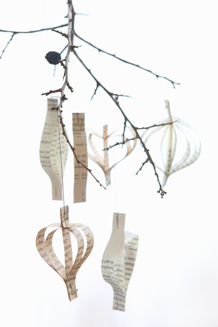 Pendants made from strips of paper hung from twig against white background