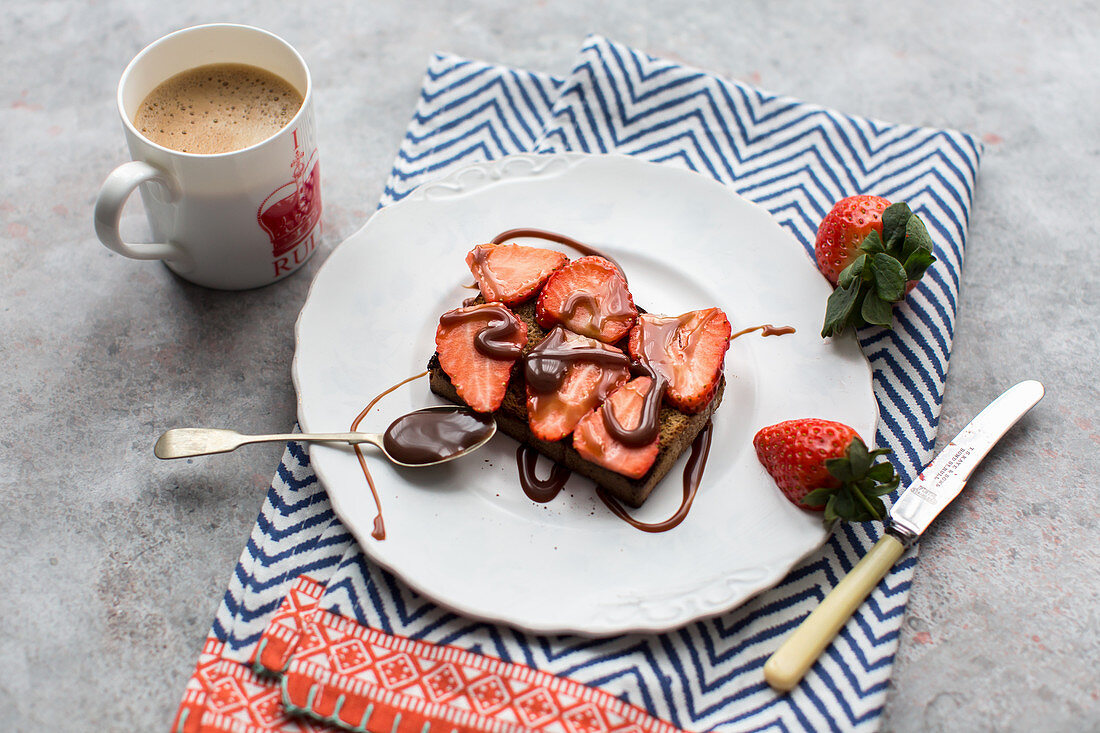 A slice of rye bread topped with strawberries and drizzled with chocolate sauce