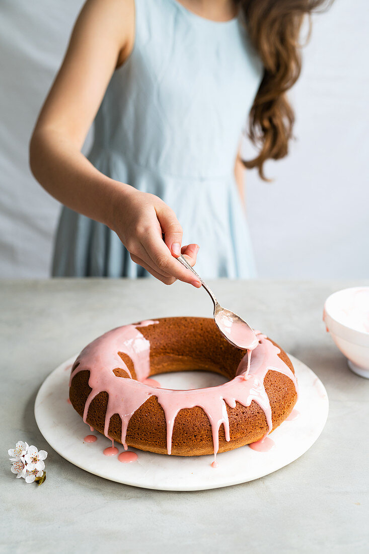 A girl glazing a cake with pink icing
