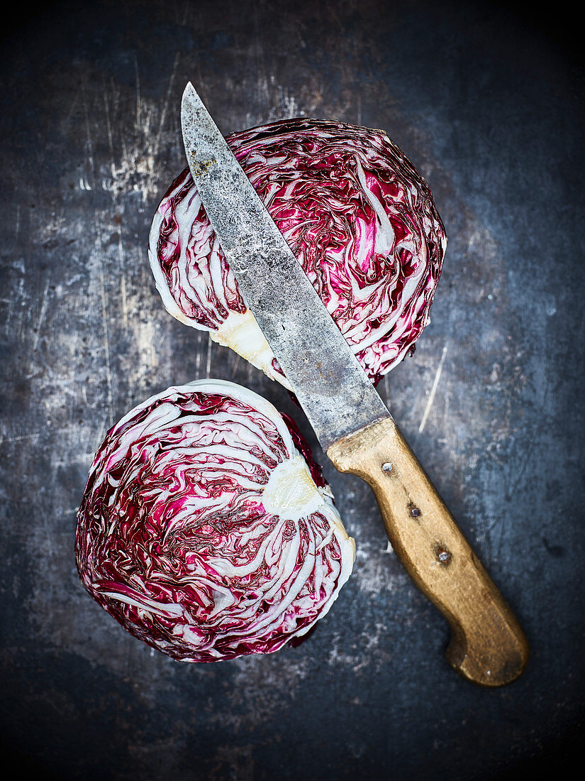 A halved radicchio with a kitchen knife on a dark metal background
