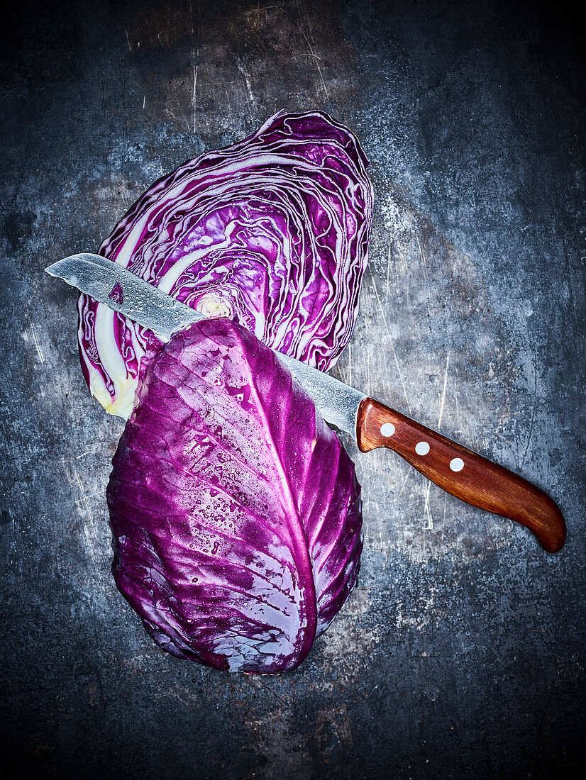 A halved red cabbage with a knife on a dark metal background