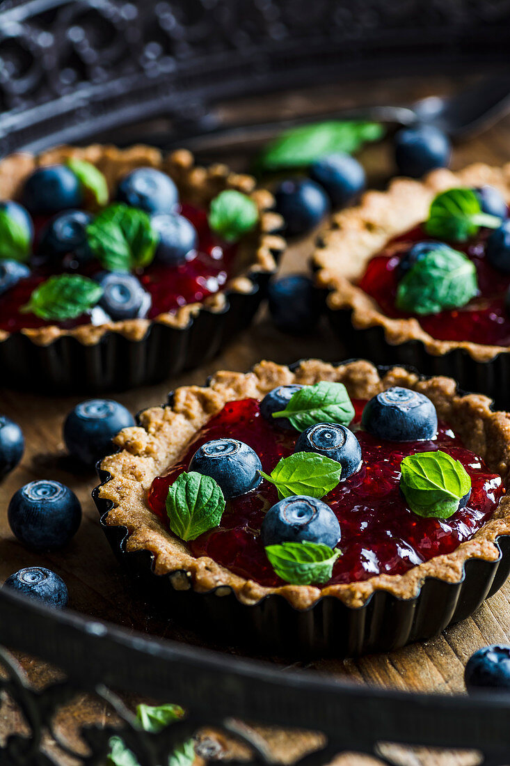 Mini-Tartes mit Erdbeermarmelade und Blaubeeren, dekoriert mit Minzblättern