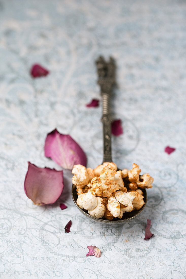 Gilded popcorn on a vintage spoon next to rose petals
