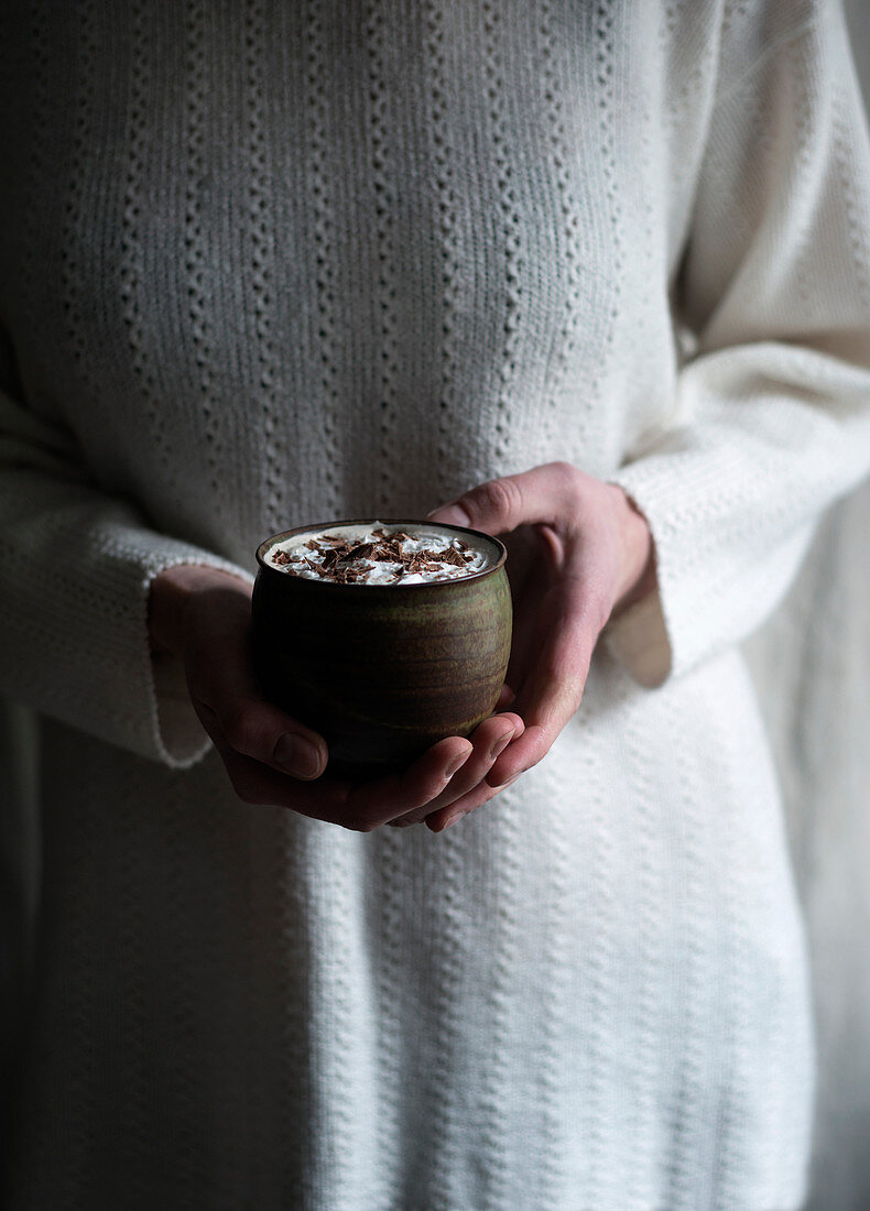A woman holding a cup of vegan hot chocolate with soy cream