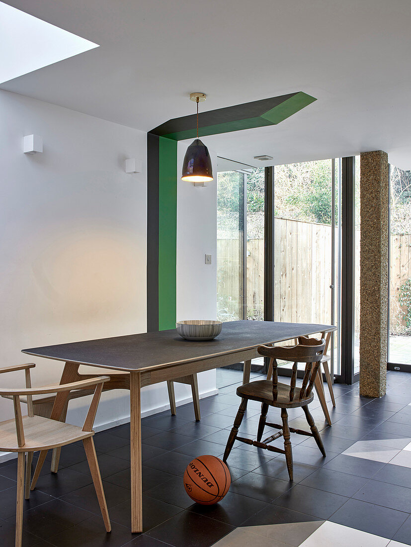 Old and new chairs around dining table next to graphic painted accent on wall