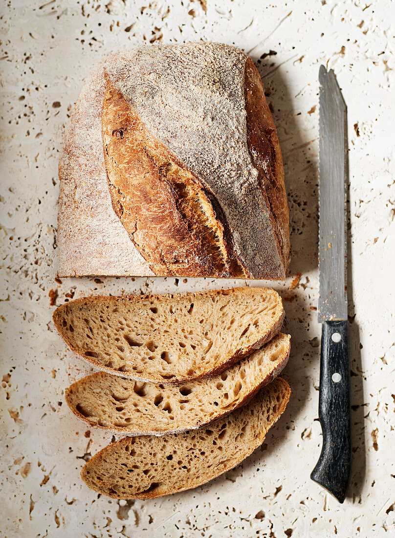 A sourdough loaf sliced sitting on a stone surface