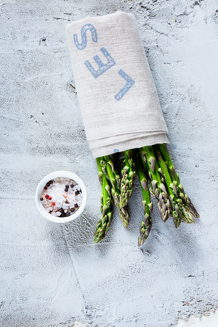 Fresh green asparagus wrapped in a cloth, with a bowl of spices