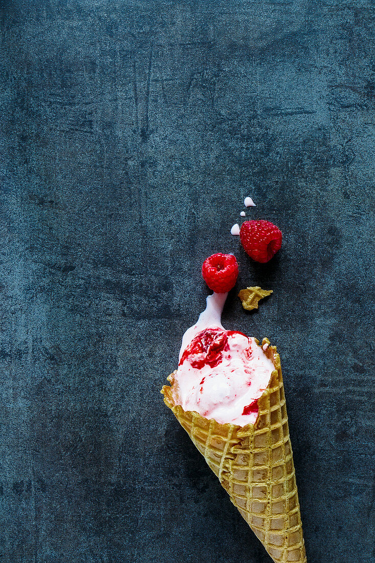 Himbeereis im Waffelhörnchen auf blaugrauem Untergrund (Aufsicht)