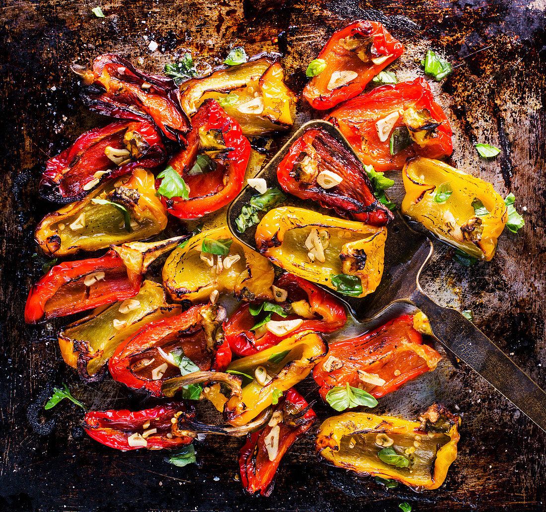Roasted peppers with garlic and basil on an oven tray (top view)