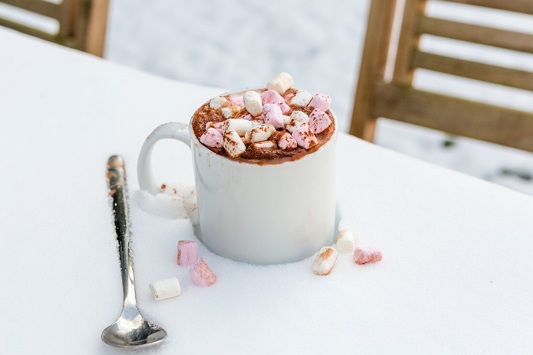 A cup of hot chocolate with marshmallows on a table in the snow