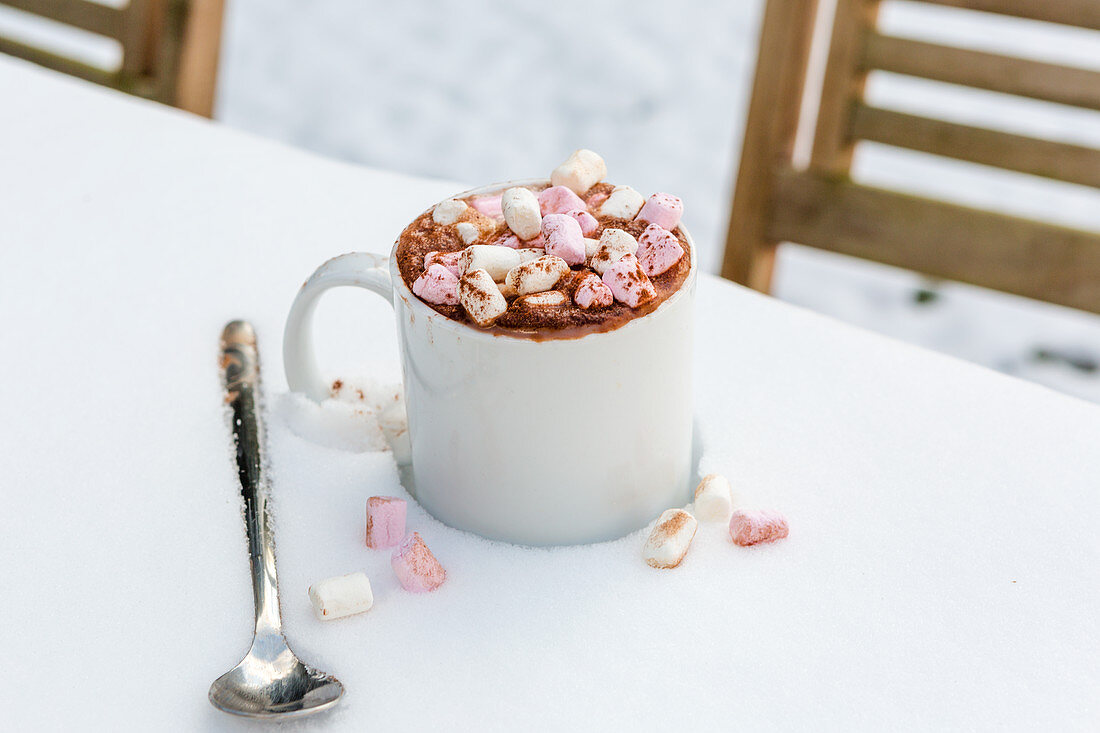 Ein Becher heiße Schokolade mit Marshmallows auf Tisch im Schnee