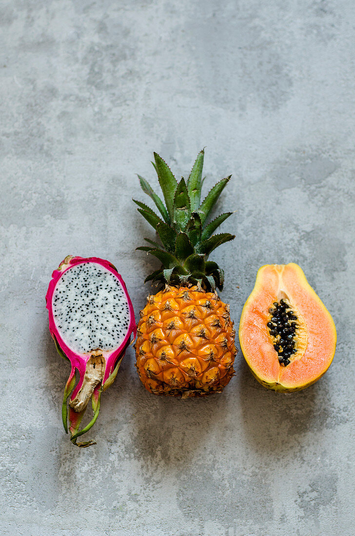 A pitahaya, a baby pineapple and a papaya all halved