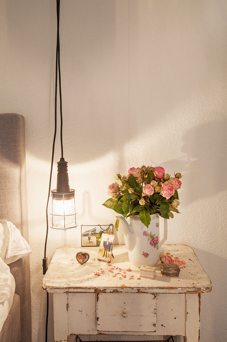Bouquet of roses in coffee jug on old bedside table