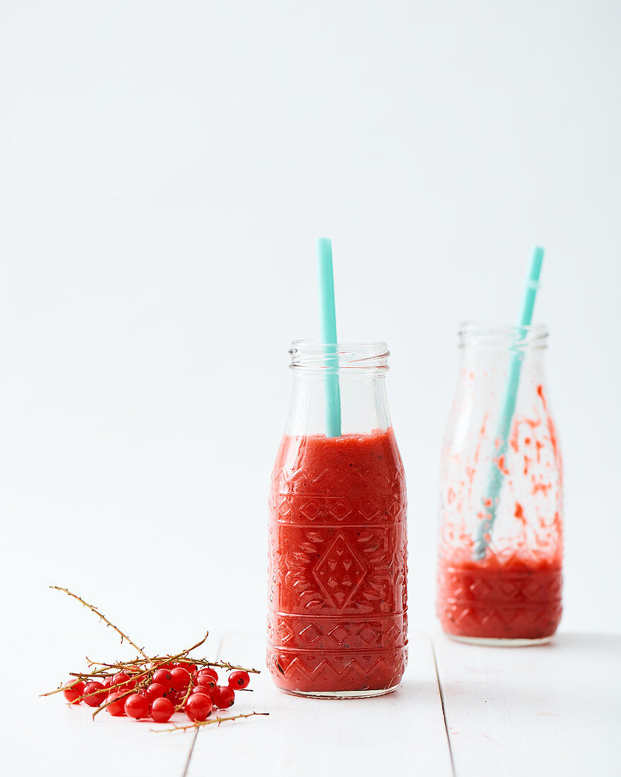 Rote Johannisbeersmoothies in Glasflasche mit Strohhalm