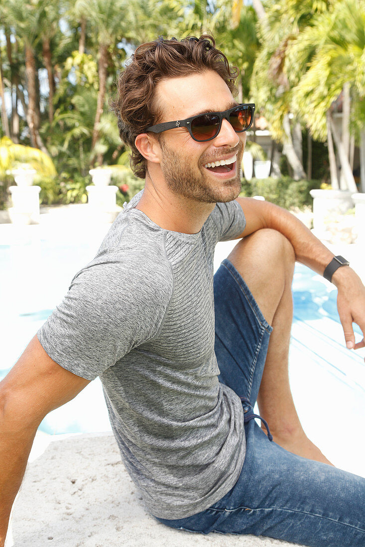 Junger Mann mit Sonnenbrille in grauem T-Shirt und Jeans-Bermuda