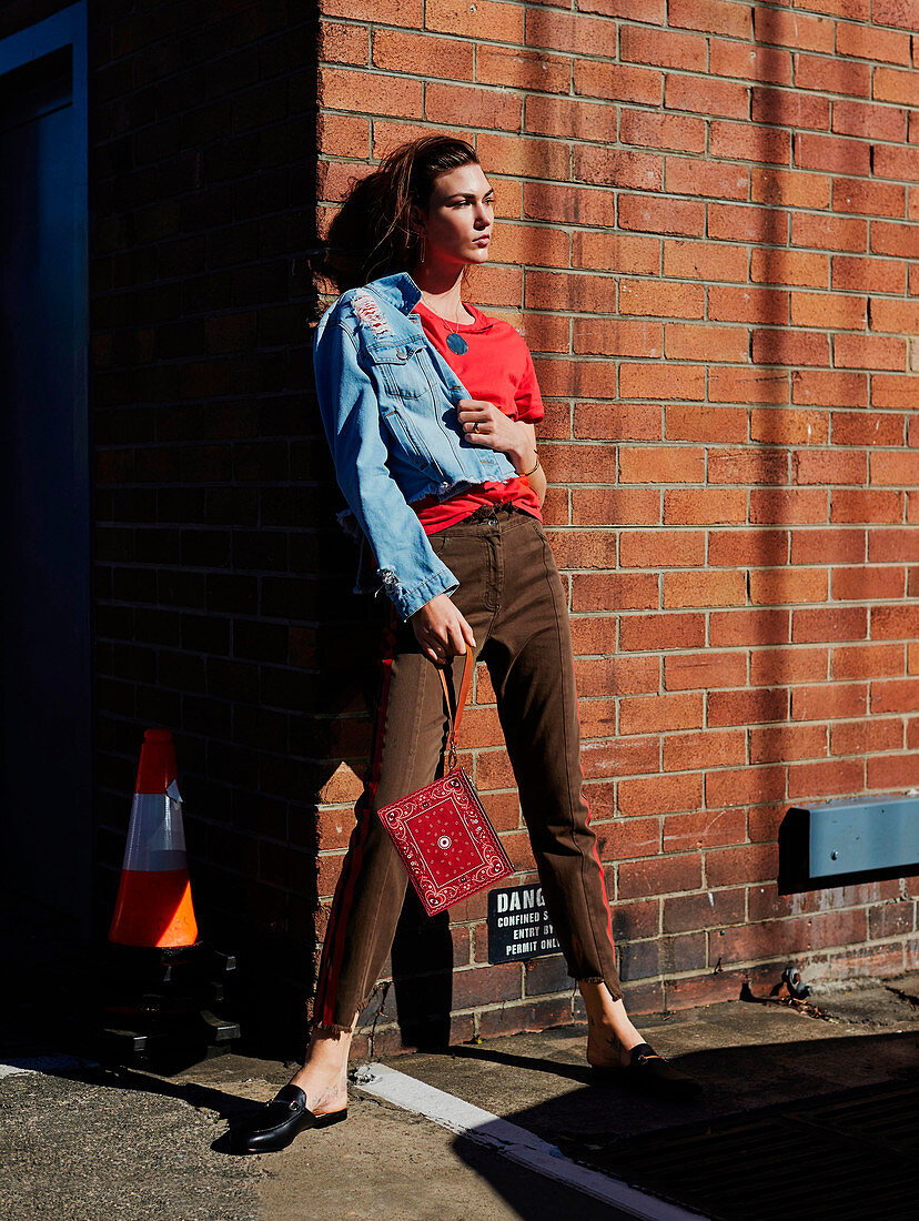 A brunette woman wearing a red t-shirt, a denim jacket and brown trousers