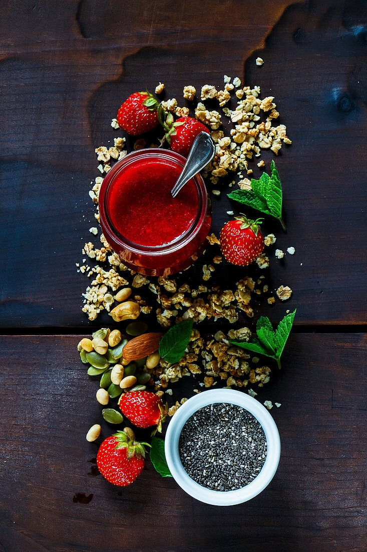 Freshly made strawberry puree, chia seeds, granola, fresh berries and mint for breakfast or smoothie. Healthy ingredients on dark wooden background